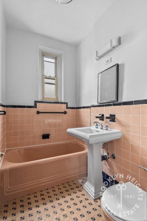 full bath with toilet, a wainscoted wall, tile walls, and a bath