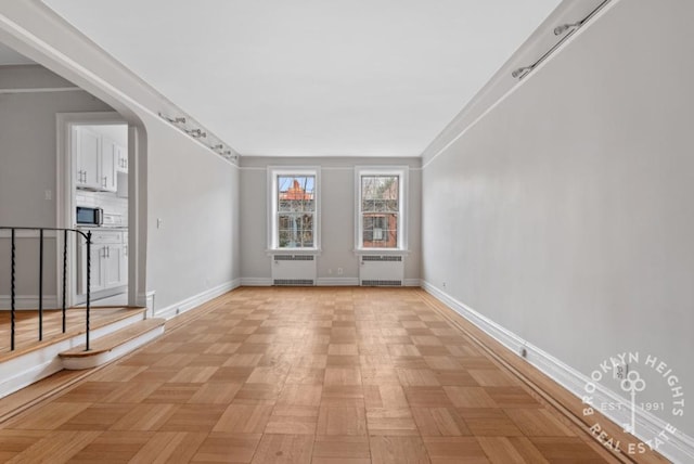 unfurnished living room with arched walkways, baseboards, and radiator