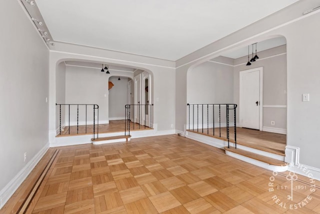 empty room featuring arched walkways, baseboards, and stairs