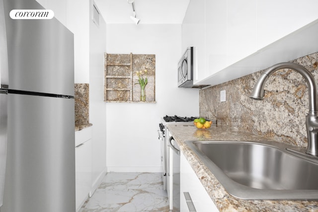 kitchen with tasteful backsplash, appliances with stainless steel finishes, marble finish floor, white cabinetry, and a sink