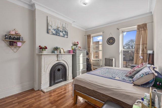 bedroom with baseboards, radiator heating unit, a fireplace with flush hearth, ornamental molding, and wood finished floors