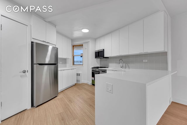 kitchen featuring light wood-style flooring, appliances with stainless steel finishes, light countertops, white cabinetry, and a sink