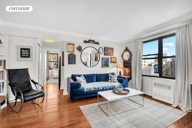 living area with radiator heating unit, crown molding, visible vents, and wood finished floors