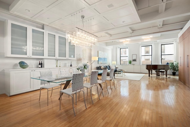 dining space with light wood-style flooring, a chandelier, and coffered ceiling