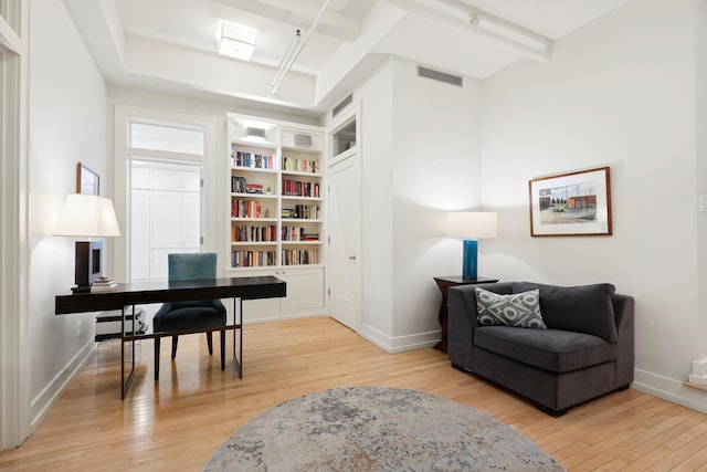 office featuring visible vents, light wood-type flooring, built in shelves, beam ceiling, and baseboards