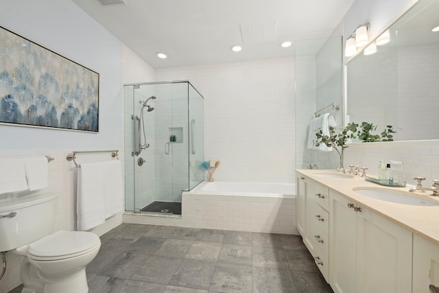 bathroom with a sink, tile walls, a stall shower, and toilet