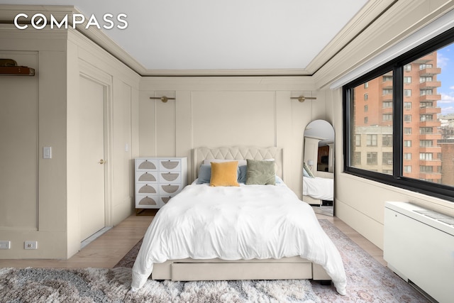 bedroom featuring a decorative wall, light wood-style flooring, radiator, and crown molding