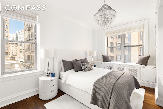 bedroom with baseboards, dark wood finished floors, a city view, crown molding, and a notable chandelier