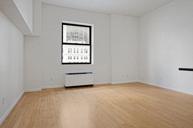 unfurnished room featuring baseboards, light wood-style flooring, and radiator heating unit