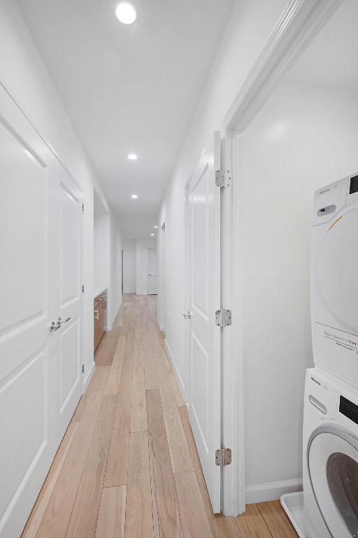 corridor featuring stacked washer and dryer, recessed lighting, light wood-style floors, and baseboards