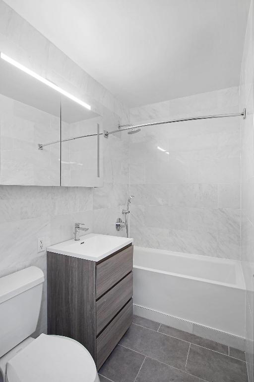 full bathroom with bathing tub / shower combination, toilet, tile patterned flooring, vanity, and tile walls