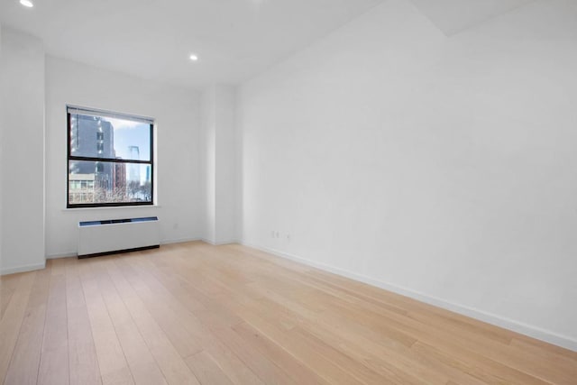 empty room featuring light wood-type flooring, radiator heating unit, baseboards, and recessed lighting