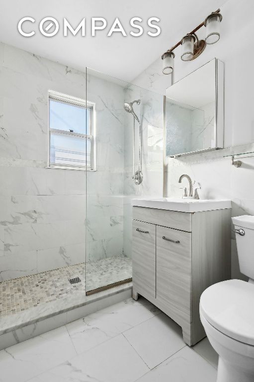 bathroom with marble finish floor, tile walls, a marble finish shower, toilet, and vanity