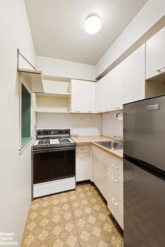 kitchen with white cabinets, freestanding refrigerator, white gas range, light countertops, and a sink