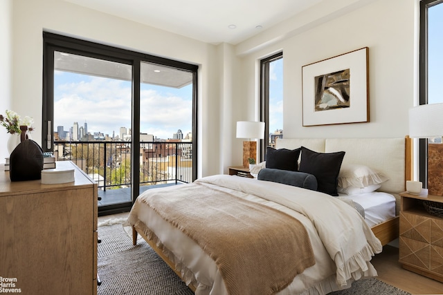 bedroom with access to outside, a skyline view, multiple windows, and wood finished floors