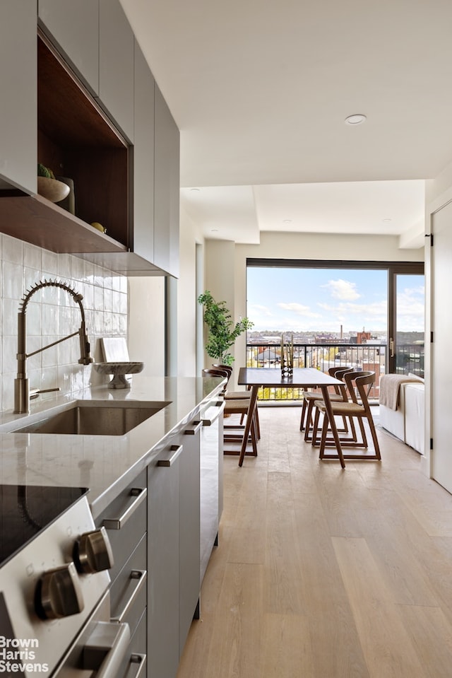 kitchen with a sink, modern cabinets, light wood finished floors, stone countertops, and gray cabinetry