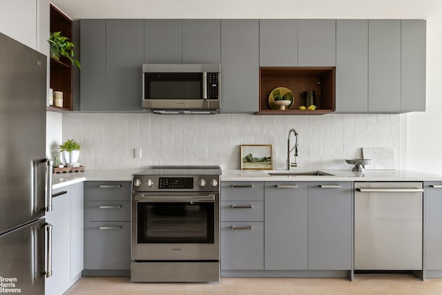kitchen featuring stainless steel appliances, gray cabinets, a sink, and open shelves