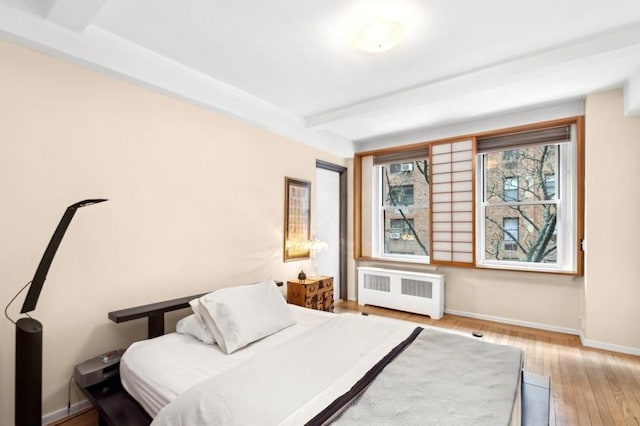 bedroom featuring light wood finished floors, radiator heating unit, baseboards, and beam ceiling