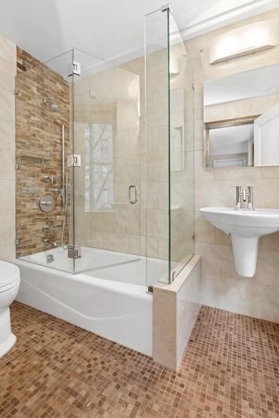 bathroom featuring combined bath / shower with glass door, tile patterned flooring, toilet, and tile walls