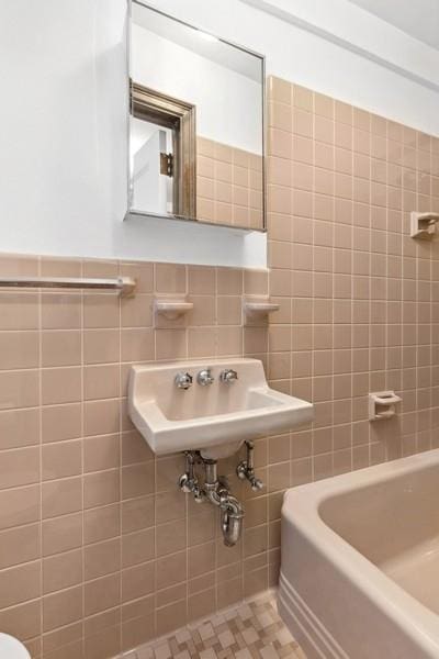 full bathroom featuring a wainscoted wall, a bathtub, a sink, and tile walls