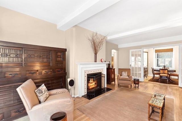 sitting room featuring light wood finished floors, a tiled fireplace, beam ceiling, and baseboards