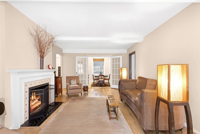 living room with a fireplace with flush hearth, light wood-type flooring, and beamed ceiling