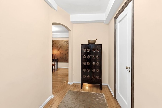 hall with light wood finished floors, baseboards, and arched walkways