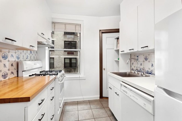 kitchen with light tile patterned floors, under cabinet range hood, white appliances, a sink, and white cabinets