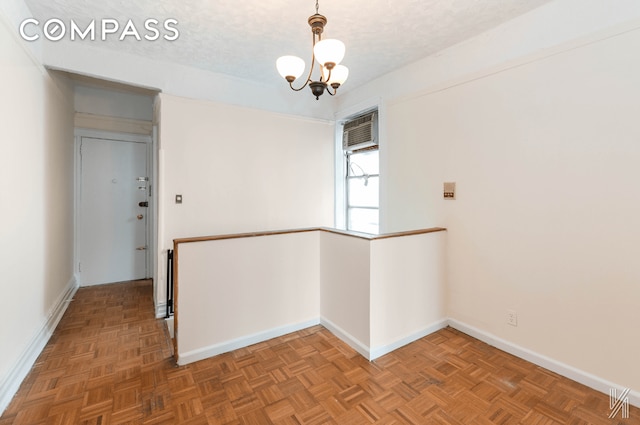 unfurnished room with a notable chandelier, baseboards, and a textured ceiling