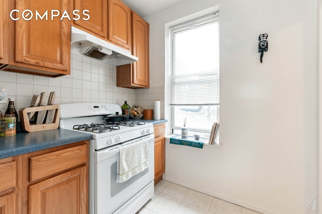 kitchen with tasteful backsplash, dark countertops, brown cabinets, under cabinet range hood, and gas range gas stove