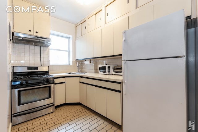 kitchen with light countertops, backsplash, a sink, white appliances, and under cabinet range hood