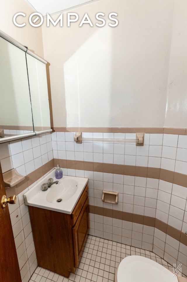 half bath with wainscoting, toilet, tile patterned floors, vanity, and tile walls