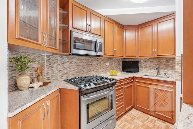 kitchen with light stone countertops, stainless steel appliances, a sink, backsplash, and brown cabinets