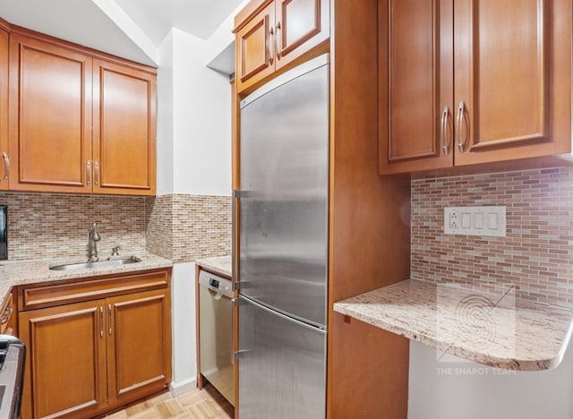 kitchen featuring stainless steel appliances, light stone counters, a sink, and brown cabinets