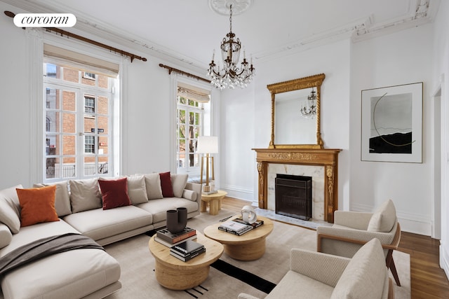 living room with a notable chandelier, a fireplace, wood finished floors, baseboards, and ornamental molding