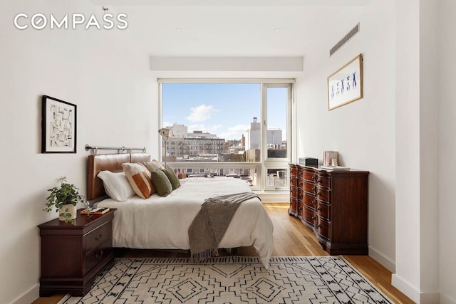 bedroom with light wood-type flooring, visible vents, a view of city, and baseboards