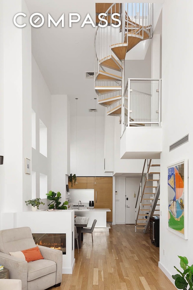 living area with light wood-style floors, visible vents, stairway, and a towering ceiling