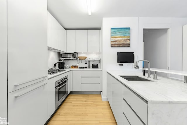 kitchen featuring a sink, light wood-style floors, stainless steel appliances, white cabinetry, and a peninsula