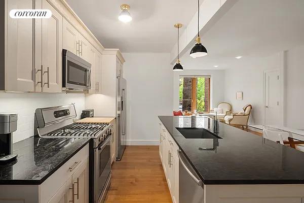 kitchen with a kitchen island with sink, a sink, white cabinets, light wood-style floors, and appliances with stainless steel finishes