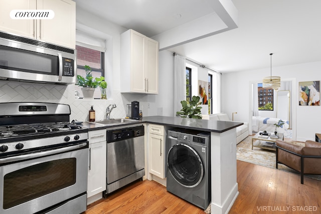 kitchen featuring open floor plan, stainless steel appliances, dark countertops, and washer / dryer