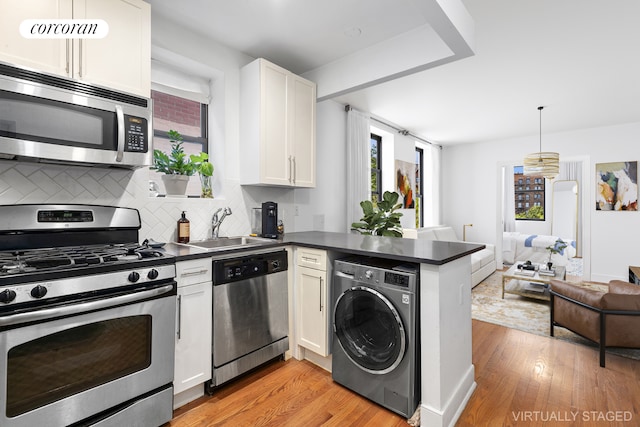 kitchen with stainless steel appliances, dark countertops, washer / clothes dryer, a sink, and a peninsula