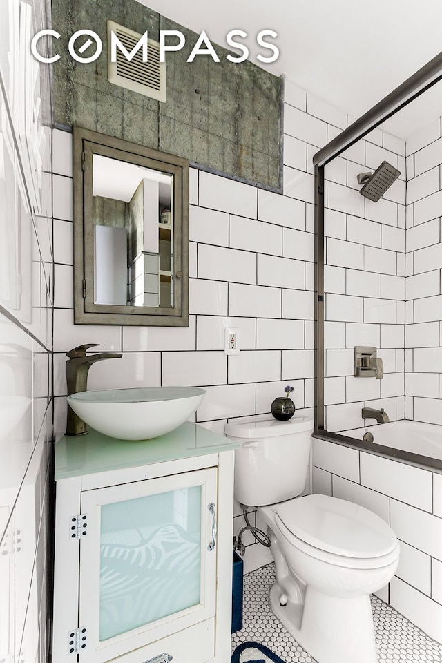 bathroom featuring tile walls, vanity, toilet, tiled shower / bath combo, and tile patterned flooring