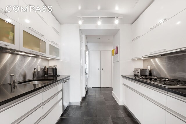 116 W 22nd St Unit 3, New York City, NY 10011 - kitchen with stainless steel appliances, dark countertops, white cabinets, rail lighting, and glass insert cabinets