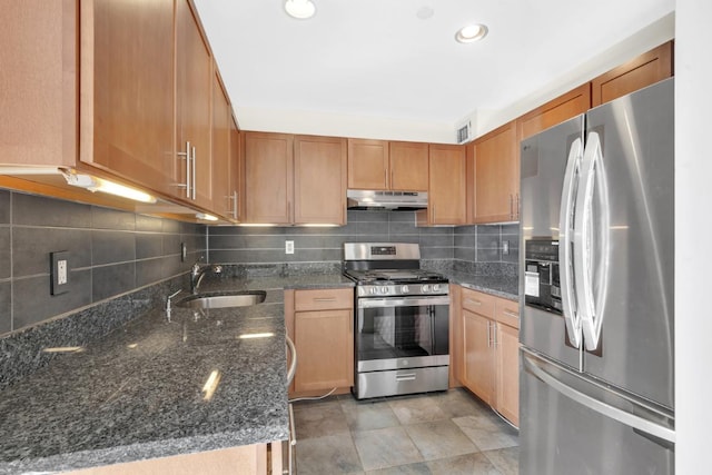 kitchen featuring appliances with stainless steel finishes, dark stone countertops, a sink, and under cabinet range hood