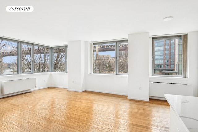 empty room with light wood-type flooring, radiator heating unit, visible vents, and baseboards