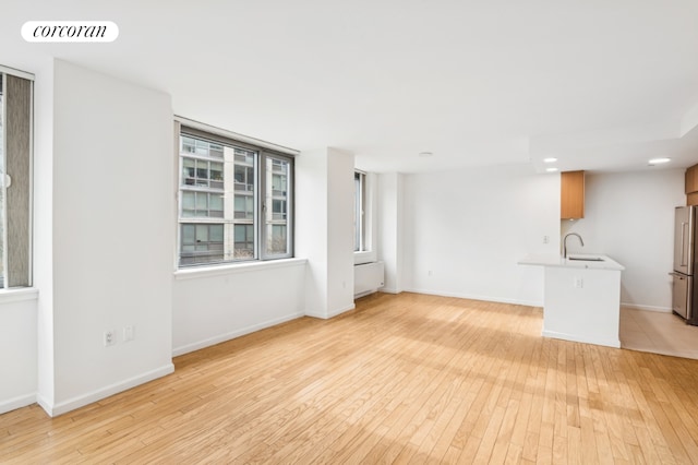 empty room with radiator, light wood-type flooring, visible vents, and baseboards