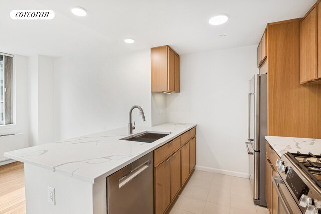 kitchen with stainless steel appliances, brown cabinetry, a sink, and light wood-style flooring