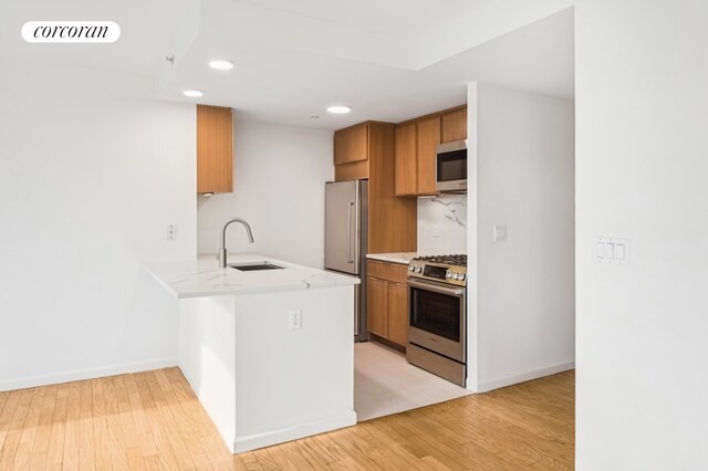 425 Main St Unit 3P, New York City, NY 10044 - kitchen with appliances with stainless steel finishes, a sink, light wood-style floors, brown cabinetry, and a peninsula