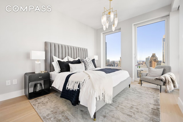 bedroom with a city view, baseboards, a notable chandelier, and wood finished floors
