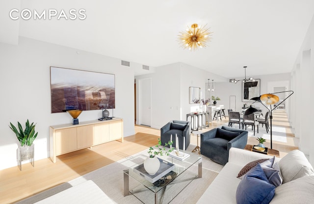 living room with stairs, an inviting chandelier, visible vents, and light wood-style floors